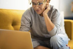 Happy Young Woman Working On Laptop Sitting On Sofa In Living Ro